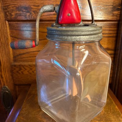 Sale Photo Thumbnail #742: This is a vintage Standard Churn Company (SCC) "Farm Master" 8-quart glass hand-crank butter churn, featuring a square jar, red-painted gear cover, and wooden paddles inside.