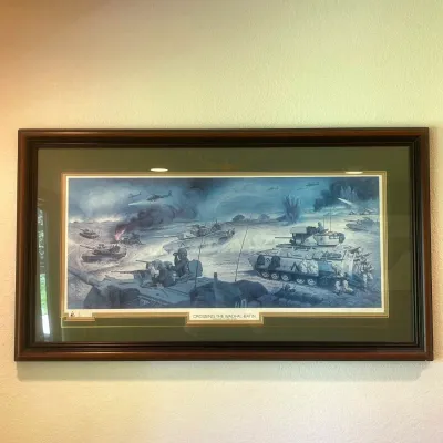 Sale Photo Thumbnail #36: Striking limited-edition military print by noted illustrator Samson Pollen, titled “Crossing the Wadi-Al-Batin – February 27, 1991, Iraq.” The detailed battlefield scene depicts U.S. armored forces during Operation Desert Storm, with tanks, armored 