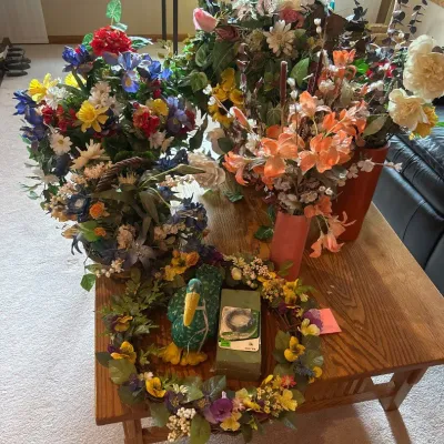 Sale Photo Thumbnail #160: A collection of beautiful floral arrangements featuring a variety of colorful artificial flowers meticulously arranged in different decorative containers. Highlights include vibrant lilies, daisies, roses, and other blooms in shades of orange, white, blue