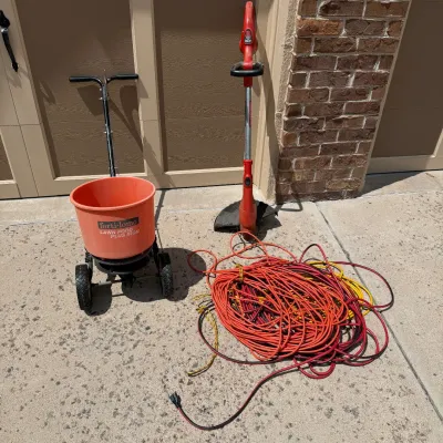 Sale Photo Thumbnail #210: This set includes a Craftsman electric trimmer, perfect for precise lawn edging and trimming tasks. Accompanied by a sturdy orange fertilizer spreader with large wheels for easy maneuverability and adjustable handle height, it ensures efficient distributi