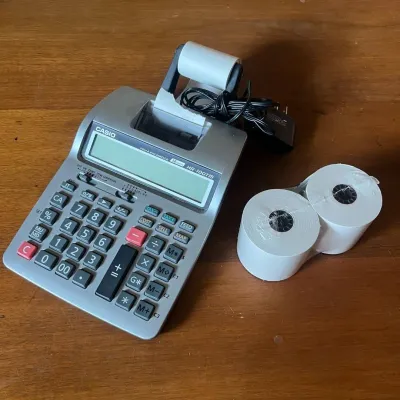 Sale Photo Thumbnail #305: This Casio HR-100TE printing calculator features a large LCD display and a built-in thermal printer for fast, easy calculations with printed records. Highlighted by its gray plastic body, this model offers a wide numeric keypad with specialized function k