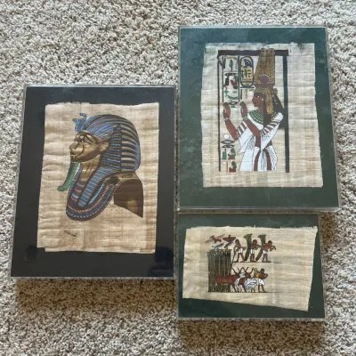 Sale Photo Thumbnail #118: This set includes three framed Egyptian papyrus artworks, each showcasing intricate depictions of ancient Egyptian culture. The artworks feature a detailed profile of a Pharaoh wearing traditional blue and gold headdress, a regal figure in white robes wit