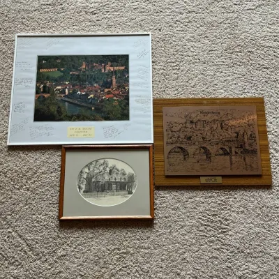 Sale Photo Thumbnail #117: This collection includes three distinct framed artworks: a vibrant aerial photograph of Heidelberg with personalized messages on the white matting, a detailed  plaque of Heidelberg mounted on a wooden backing, and a finely detailed black and white sketch 