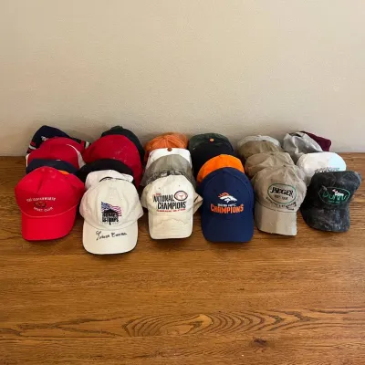 Sale Photo Thumbnail #318: This diverse assortment of 33 baseball caps features a variety of sports teams, brands, and commemorative designs. Highlights include Denver Broncos Super Bowl Champions caps in bold orange, blue, and grey tones, Texas Longhorns themed caps in white, oran