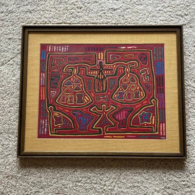 Sale Photo Thumbnail #94: Colorful vintage mola textile panel, traditionally associated with the Guna people of Panama, presented under glass with a woven-texture mat and wood-tone frame. Molas are constructed from layered fabrics that are cut and hand-sewn to reveal contrasting c