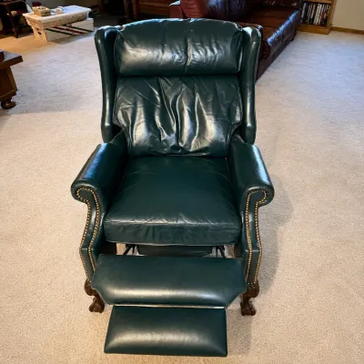 Sale Photo Thumbnail #179: This elegant dark green leather recliner chair features a classic design with rolled arms and detailed nailhead trim. Measuring 42 inches tall, 30 inches wide, and 34 inches deep when not reclined , this chair provides comfortable seating with an extendab