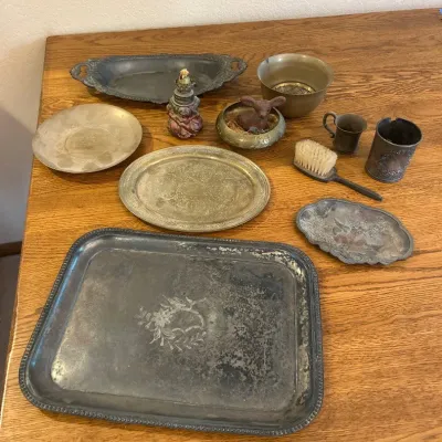 Sale Photo Thumbnail #286: This unique collection of antique collectables showcases a variety of vintage metalware, including intricately designed trays with floral and patterned engravings. Highlighted by their aged patina and decorative handles, the pieces vary in size and shape,