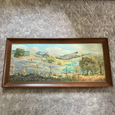 Sale Photo Thumbnail #110: Original oil landscape painting depicting a colorful rural scene with rolling hills, a winding creek, fence line, trees, distant buildings, and fields of blue and purple wildflowers. The painting features prominent hand-applied brushwork and areas of heav