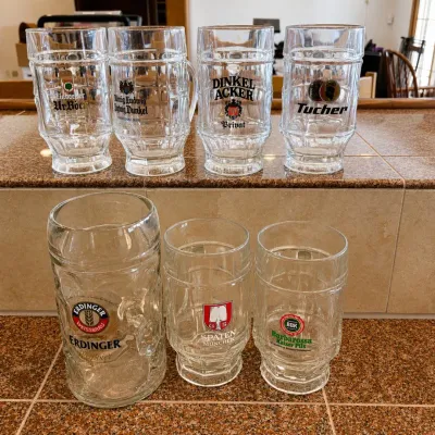 Sale Photo Thumbnail #294: This collection features 7 authentic German beer mugs, each showcasing logos from various renowned breweries including Eichbaum, Lepat Privat, Dinkel Acker, Tucher, Erdinger, Spaten Munchen, and Barbarossa. The set includes mugs ranging in size from appro