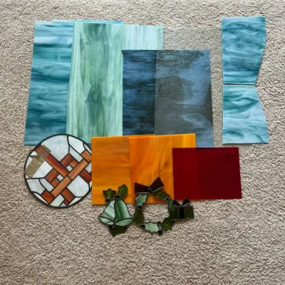 Sale Photo Thumbnail #321: This collection features an assortment of 14 stained glass pieces showcasing a variety of swirling colors including shades of green, blue, orange, and red. The set includes several large sheets of glass with fluid, marbled patterns in green and blue hues,
