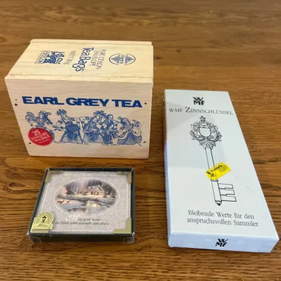 Sale Photo Thumbnail #151: This diverse collection of collector's items features a vintage wooden box of Earl Grey Tea adorned with classic blue illustrations. Included is a decorative plaque with a serene winter cabin scene and a heartfelt message, elegantly framed with gold-color