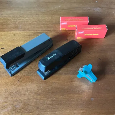 Sale Photo Thumbnail #304: This office supply set features two full-sized staplers in black and grey, each designed for reliable and efficient document fastening. Included are two boxes of standard red-packaged staples, each containing 5000 staples, suitable for frequent use. Addit
