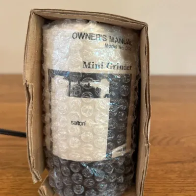 Sale Photo Thumbnail #242: This Salton Mini Grinder features a compact and portable design, perfect for small grinding tasks. The unit is securely wrapped in bubble wrap and packaged in its original cardboard box for protection. It measures approximately 7.5 inches tall, making it 