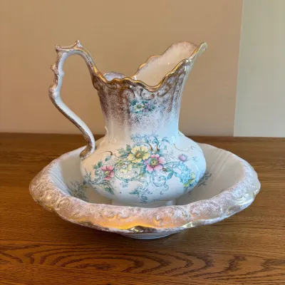 Sale Photo Thumbnail #24: This elegant porcelain wash pitcher and basin set features intricate floral designs complemented by luxurious gold trim. The pitcher stands 14 inches tall and is 9 inches wide, while the basin measures 4.5 inches in height and 15.5 inches in width. Both p