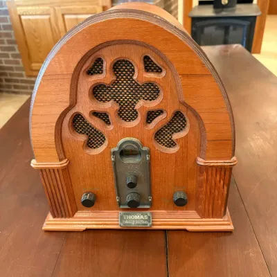 Sale Photo Thumbnail #70: This Thomas Collector's Edition Radio, Model 217, offers a charming vintage aesthetic with its classic wooden casing and intricate front grille design. Measuring 12.5 inches tall, 11.5 inches wide, and 8 inches deep, this radio features a warm wood finish