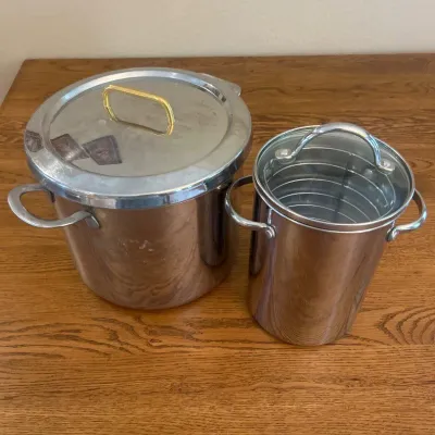 Sale Photo Thumbnail #232: This stainless steel cookware set features two essential pieces designed for versatile cooking. The set includes a large pot with a secure lid that has a gold-tone handle for easy lifting, and a smaller tall pot with dual handles and an inner removable ra