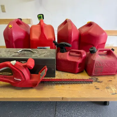 Sale Photo Thumbnail #327: This comprehensive outdoor trimmer set includes a red electric Homelite trimmer, multiple red gas cans in various sizes, and a sturdy metal toolbox. The trimmer is compact and lightweight, designed for easy handling. The gas cans, made of durable plastic,