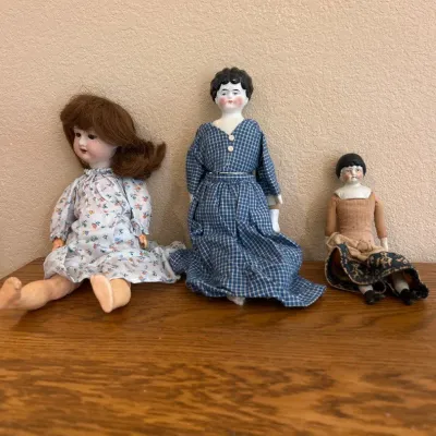Sale Photo Thumbnail #283: This charming set includes three antique ceramic dolls, each with unique hand-painted facial features and distinct clothing styles. The dolls vary in size, with the largest measuring approximately 14 inches and dressed in a delicate, floral-patterned dres