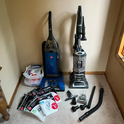 Sale Photo Thumbnail #227: This set includes two upright vacuum cleaners, featuring a blue Hoover model and a silver Shark XL capacity model. Both vacuums come with multiple attachments such as various nozzles, brushes, and hoses, enhancing their cleaning versatility. Additionally,