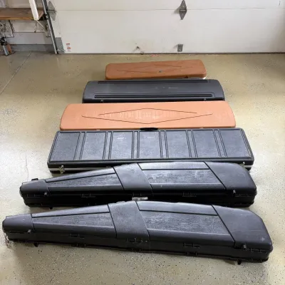 Sale Photo Thumbnail #202: This collection features an assortment of rifle cases designed to accommodate rifles of various sizes. The cases come in two primary colors: black and tan, with sturdy construction evident in the durable plastic and wood-like materials. The larger black c