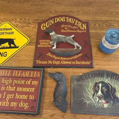Sale Photo Thumbnail #289: This Dog Lover Collection features a charming assortment of decorative items perfect for canine enthusiasts. It includes a vintage-style 'Gun Dog Tavern' sign with a detailed German Shorthaired Pointer figurine and welcoming text, a bright yellow 'German 