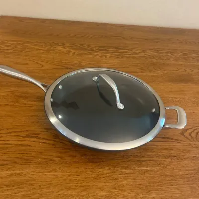 Sale Photo Thumbnail #228: This CHEFS cookware set includes a saucepan and a skillet, both crafted with durable all-clad stainless steel. The skillet features a non-stick black cooking surface and comes with a snug-fitting glass lid with a stainless steel handle. The skillet measur