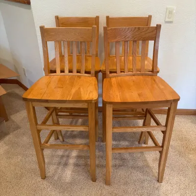 Sale Photo Thumbnail #193: This set of four bar stools features sturdy wooden construction with a natural finish, highlighting the warm honey-toned wood grain. Each stool includes a supportive backrest that measures 43.5 inches tall and a seat height of 30 inches, providing comfort