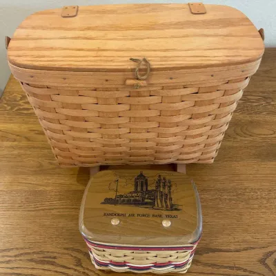 Sale Photo Thumbnail #150: This set features two unique Longaberger baskets known for their handcrafted quality and classic woven wood design. The larger basket showcases a natural wood finish with a sturdy latch and is elevated on small wooden feet. Accompanying it is a smaller, p