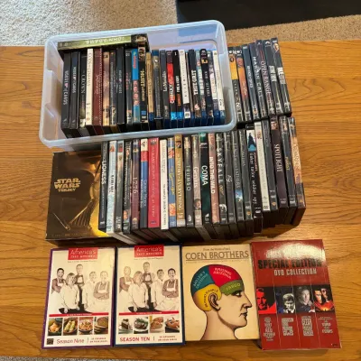 Sale Photo Thumbnail #215: This extensive collection of DVDs and Blu-rays features a wide assortment of movies and TV series spanning various genres. Included are popular titles and box sets such as 'House of Cards,' 'The Crown,' 'True Grit,' 'Spotlight,' and more. The discs are ne