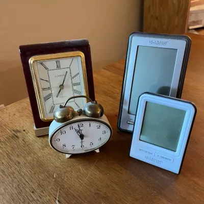 Sale Photo Thumbnail #317: This collection features four distinctive desktop clocks, blending vintage charm with modern technology. Included is a classic Linden clock with a rich mahogany wooden frame, gold trim, and an elegant white face with Roman numerals, perfect for a traditio