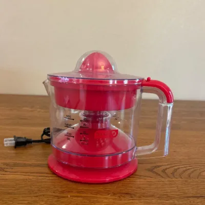 Sale Photo Thumbnail #245: This Dash Electric Citrus Juicer offers a convenient and efficient way to extract juice from citrus fruits. Featuring a clear plastic pitcher with measurement markings, it allows you to see the juice level as you press. The juicer is compact in size, easy