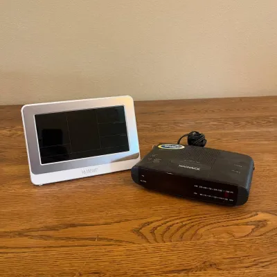 Sale Photo Thumbnail #320: This set includes a compact black MAGNAVOX clock radio with AM/FM functionality and an attached power cord, complemented by a separate white digital La Crosse display screen. The display screen boasts a modern rectangular shape with a black screen and whi