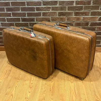 Sale Photo Thumbnail #223: This vintage suitcase set features two sturdy hard shell suitcases in a rich, warm brown color with a textured finish. The cases are accented with shiny chrome hardware, including a robust locking mechanism, metal trim, and comfortable leather-wrapped han