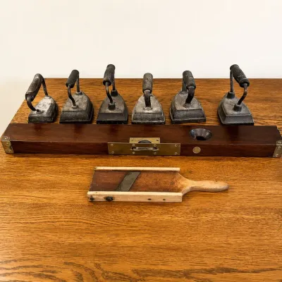 Sale Photo Thumbnail #157: This unique collection features six small antique irons, each with a distinct handle design, crafted from metal and showing natural patina and wear indicative of their age. Included is a vintage level made of rich dark wood and a wooden-handled mandolin a