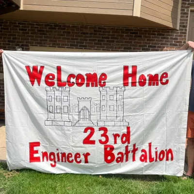 Sale Photo Thumbnail #56: This large white fabric banner (65in x 95in) features bold red lettering that reads 'Welcome Home 23rd Engineer Battalion' with an outlined sketch of a historic castle at the center. The banner is designed to celebrate and honor the 23rd Engineer Battalio
