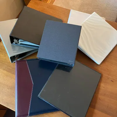 Sale Photo Thumbnail #315: This assortment features a variety of three-ring binders in multiple colors including black, white, navy blue with burgundy accents, and gray. The binders showcase different cover materials such as matte plastic, glossy plastic, textured fabric, and leath