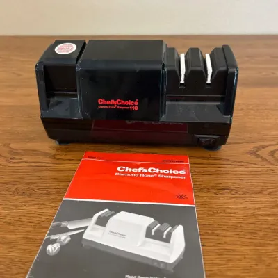 Sale Photo Thumbnail #241: This Chef'sChoice Diamond Hone Electric Knife Sharpener Model 110 is a compact and efficient kitchen tool designed to sharpen knives with precision. Featuring a black durable plastic body and a three-stage sharpening system, it ensures professional-grade 