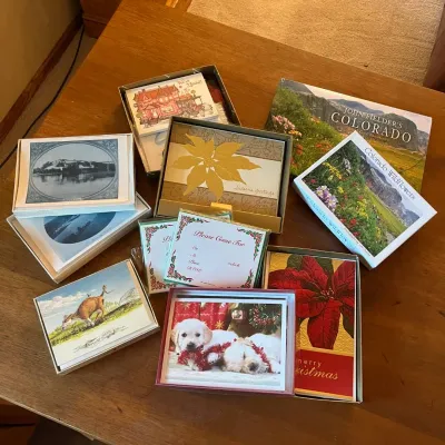 Sale Photo Thumbnail #314: This diverse collection features multiple sets of cards, each presented in unique, decorative boxes. Included are charming designs such as vintage black-and-white photographs, colorful nature and wildlife scenes including flowers and a cow, as well as fes