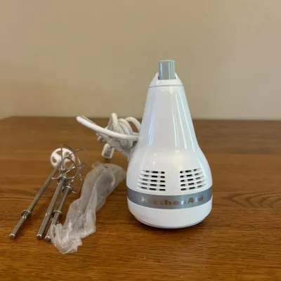 Sale Photo Thumbnail #250: This KitchenAid K-247 hand mixer features a classic white finish and a compact, ergonomic design measuring approximately 7 inches in length. It includes dual stainless steel beaters, ideal for efficiently mixing batter, dough, and other ingredients. The h