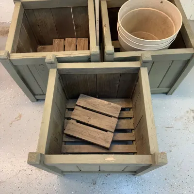 Sale Photo Thumbnail #326: Set of wooden crates designed for use as planters, each including small pallets inside and pots. These crates are constructed from sturdy wood with a rustic finish, featuring a greenish tone. The dimensions are approximately 19 inches in height and 18.25 