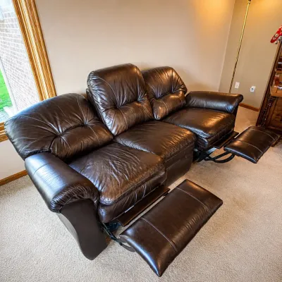 Sale Photo Thumbnail #178: This La-Z-Boy reclining couch features rich dark brown leather upholstery, offering both comfort and style. Designed to seat three, it includes two reclining seats with footrests for ultimate relaxation. The couch measures 40 inches tall, 87 inches wide, 