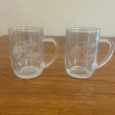 Sale Photo Thumbnail #267: This set includes two clear glass mugs featuring the Bass Pro Shops logo etched on the front. Each mug measures approximately 3.5 inches in height and 3.25 inches in diameter. Crafted from transparent glass, these mugs are perfect for enjoying your favori