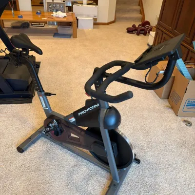 Sale Photo Thumbnail #221: This Pro-Form Sport CX indoor exercise bike features a sleek, modern design with a sturdy black and gray frame. It includes an adjustable digital console for tracking your workout metrics and a red resistance knob for easy intensity adjustments. The bike 