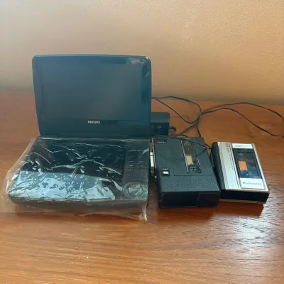 Sale Photo Thumbnail #71: This lot includes a Philips PET941A/37 portable MP3 and DVD video player, featuring compact design and playback support for DVDs, MP3 CDs, and DivX videos. The player is black and comes with a built-in control panel. Alongside it, there is a GE cassette p