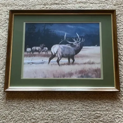 Sale Photo Thumbnail #83: Framed wildlife artwork by noted American wildlife artist Leon Parson, depicting a majestic bull elk standing before a herd in an open mountain meadow with evergreen forest and distant mountains in the background.

The artwork is signed “Leon Parson”.