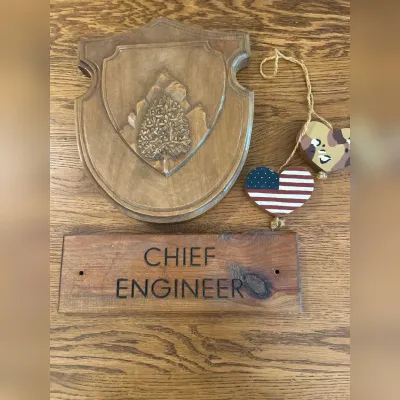 Sale Photo Thumbnail #153: This unique wooden wall decor set includes a finely carved wooden plaque with an intricately detailed tree emblem and a separate wooden sign engraved with 'CHIEF ENGINEER.' The decor pieces showcase a rich, natural wood finish highlighting the beautiful g