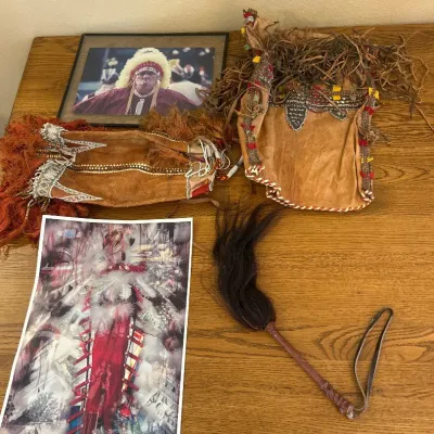 Sale Photo Thumbnail #276: This unique American Indian decor collection includes a variety of handcrafted items such as an intricately designed leather pouch adorned with detailed beadwork and fringe, a traditional feathered ceremonial accessory, and a striking printed artwork depi