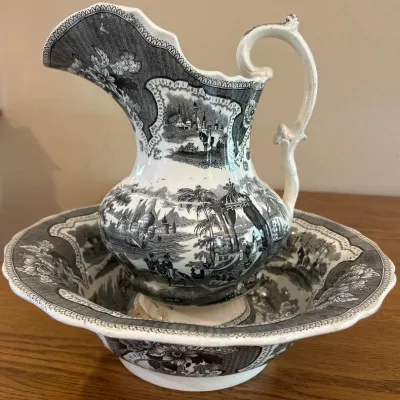 Sale Photo Thumbnail #287: This exquisite antique wash set features a matching basin and pitcher adorned with intricate black and white transferware scenes depicting pastoral and architectural elements. The ceramic pieces showcase finely detailed floral borders and classic 19th-cen