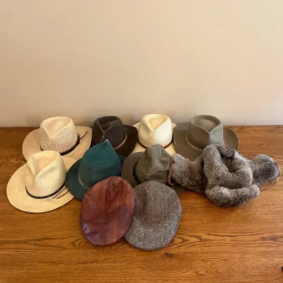 Sale Photo Thumbnail #319: This assortment includes ten distinctive hats showcasing a variety of styles such as classic Panama hats, rugged felt fedoras, a teal-colored fedora, a brown leather flat cap, a grey tweed flat cap, and a luxurious grey fur hat. Highlighting a range of co