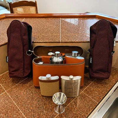 Sale Photo Thumbnail #290: This vintage travel bar set features a stylish brown leather case containing multiple stainless steel flasks and a portable wine carrier. Included are two flasks, one with a fabric-covered exterior and another engraved with detailed text, along with a sma